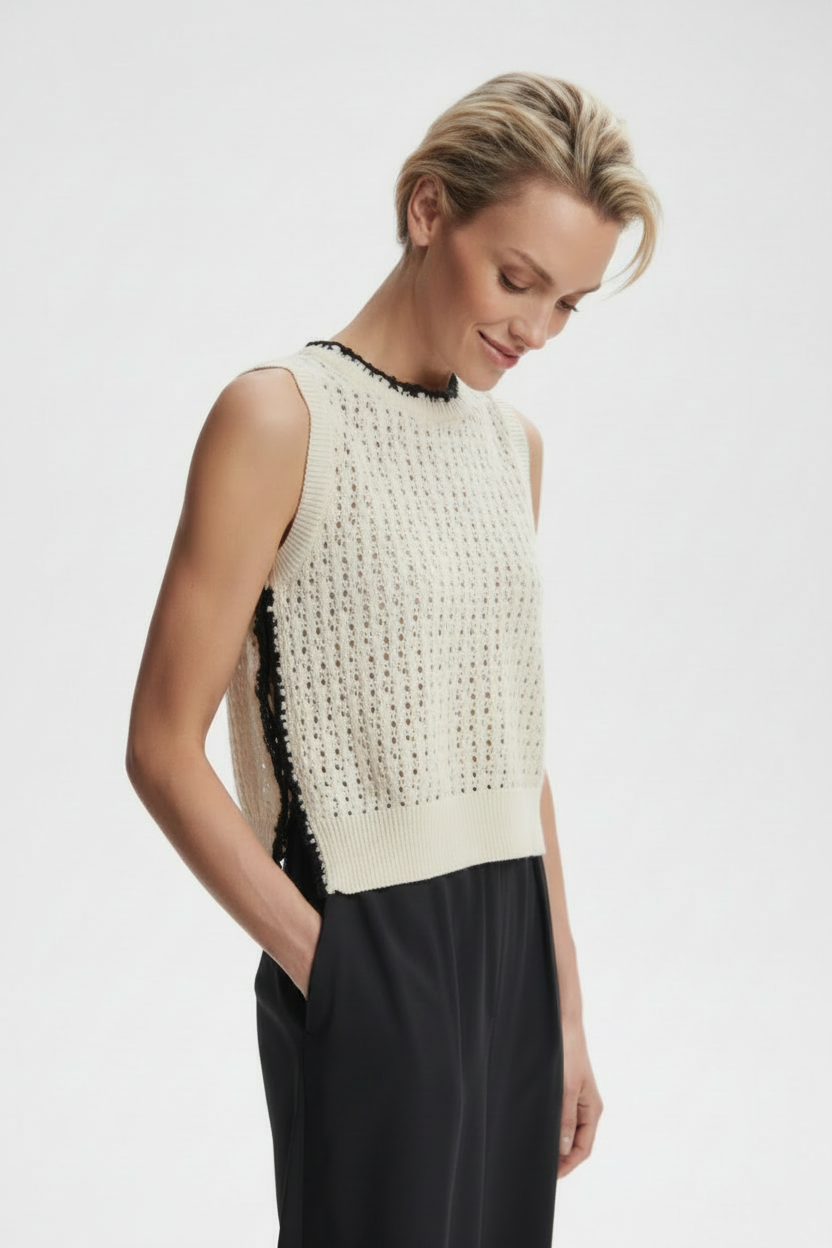 Woman wearing a sleeveless cream top with black beading on a white background
