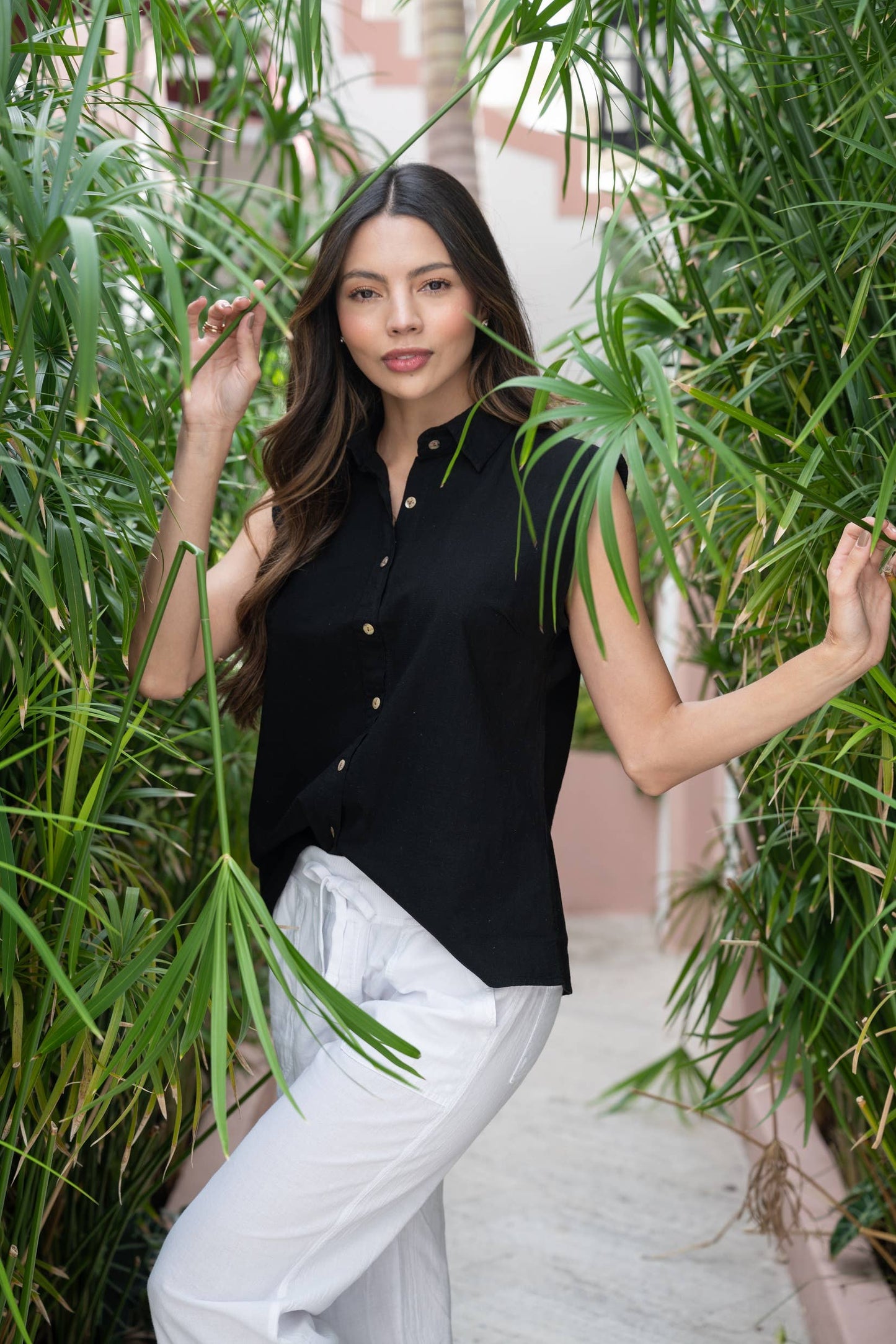 Woman in black sleeveless top and white pants standing among green plants