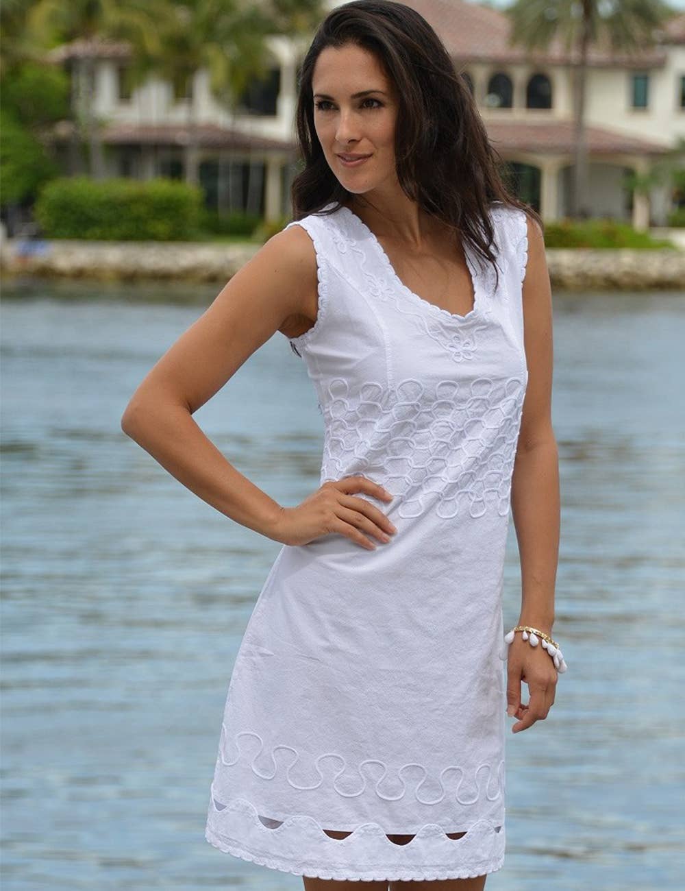 Woman wearing a white dress by a waterfront with houses and greenery in the background