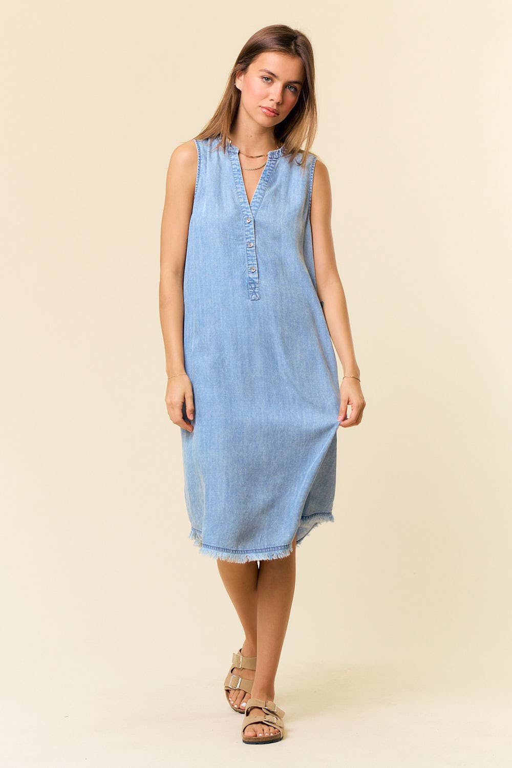 Woman wearing a light blue denim dress against a beige background