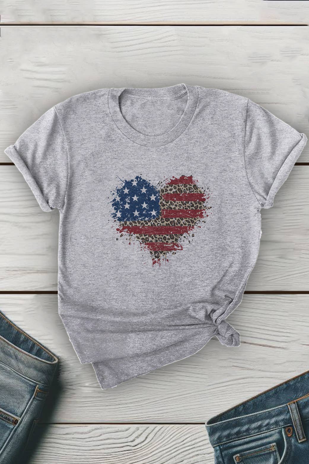 Gray t-shirt with a heart-shaped American flag design on a wooden surface with jeans.