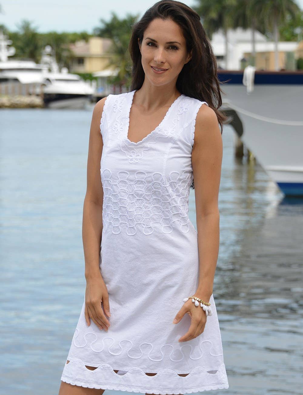 Woman wearing a white dress by a waterfront with boats in the background