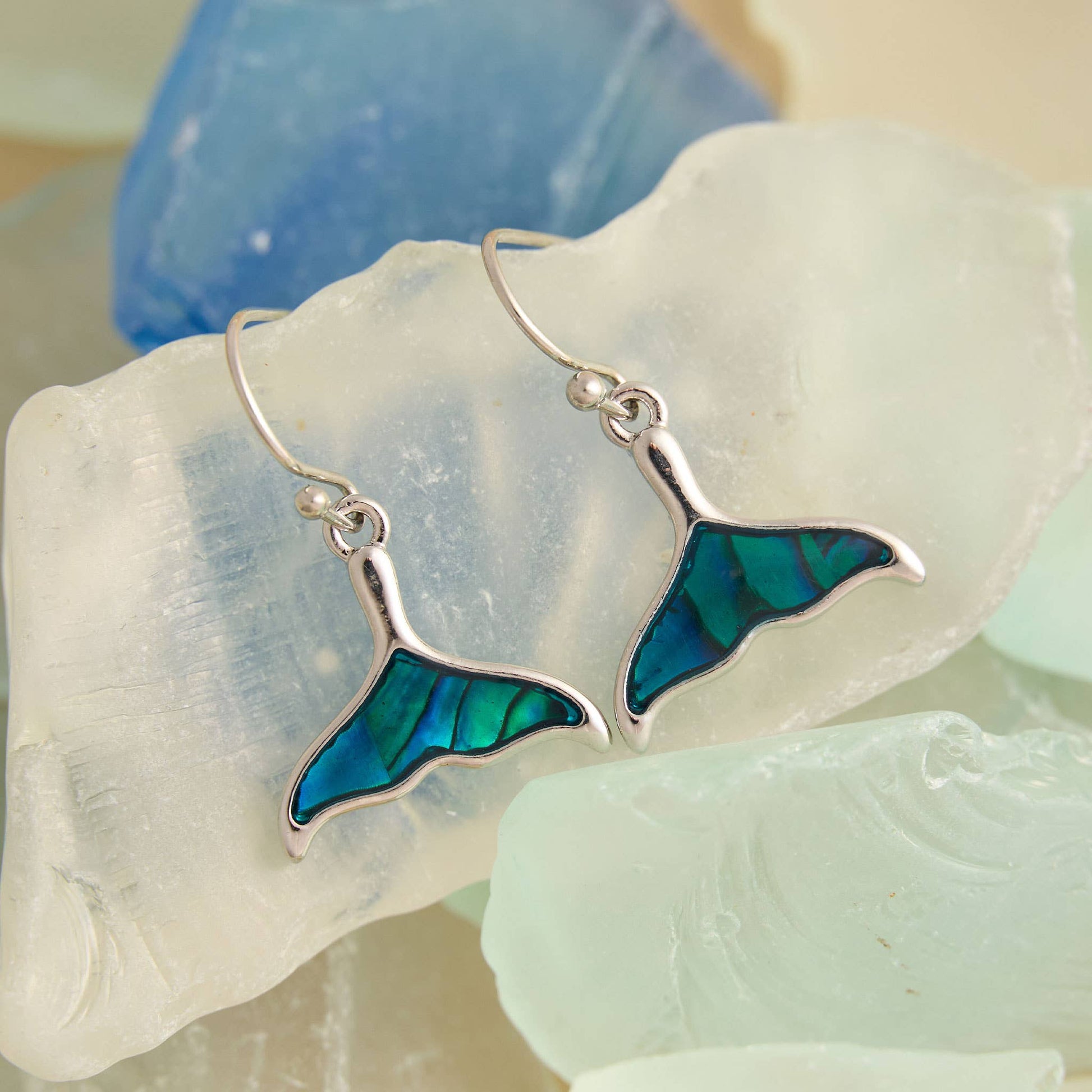 Mermaid tail earrings with blue accents on a shell background