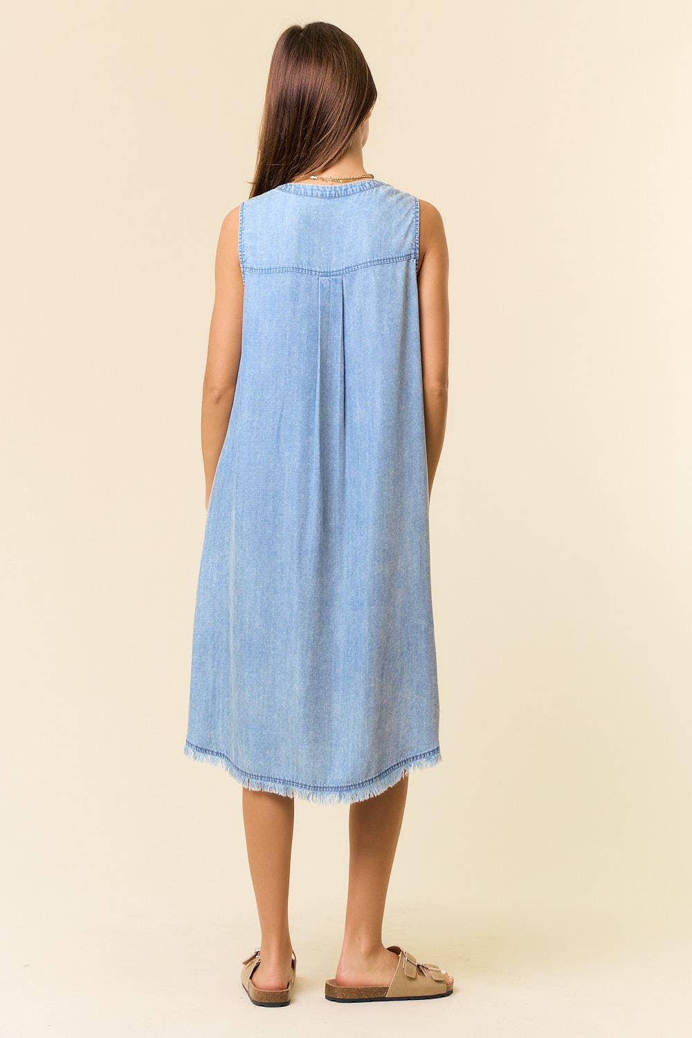 Woman wearing a light blue denim dress against a beige background