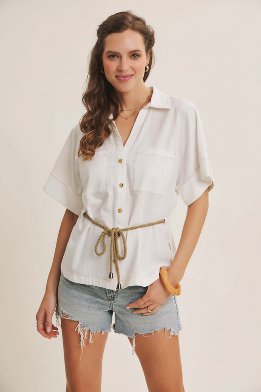 Woman wearing a white shirt with rolled-up sleeves and denim shorts on a plain background