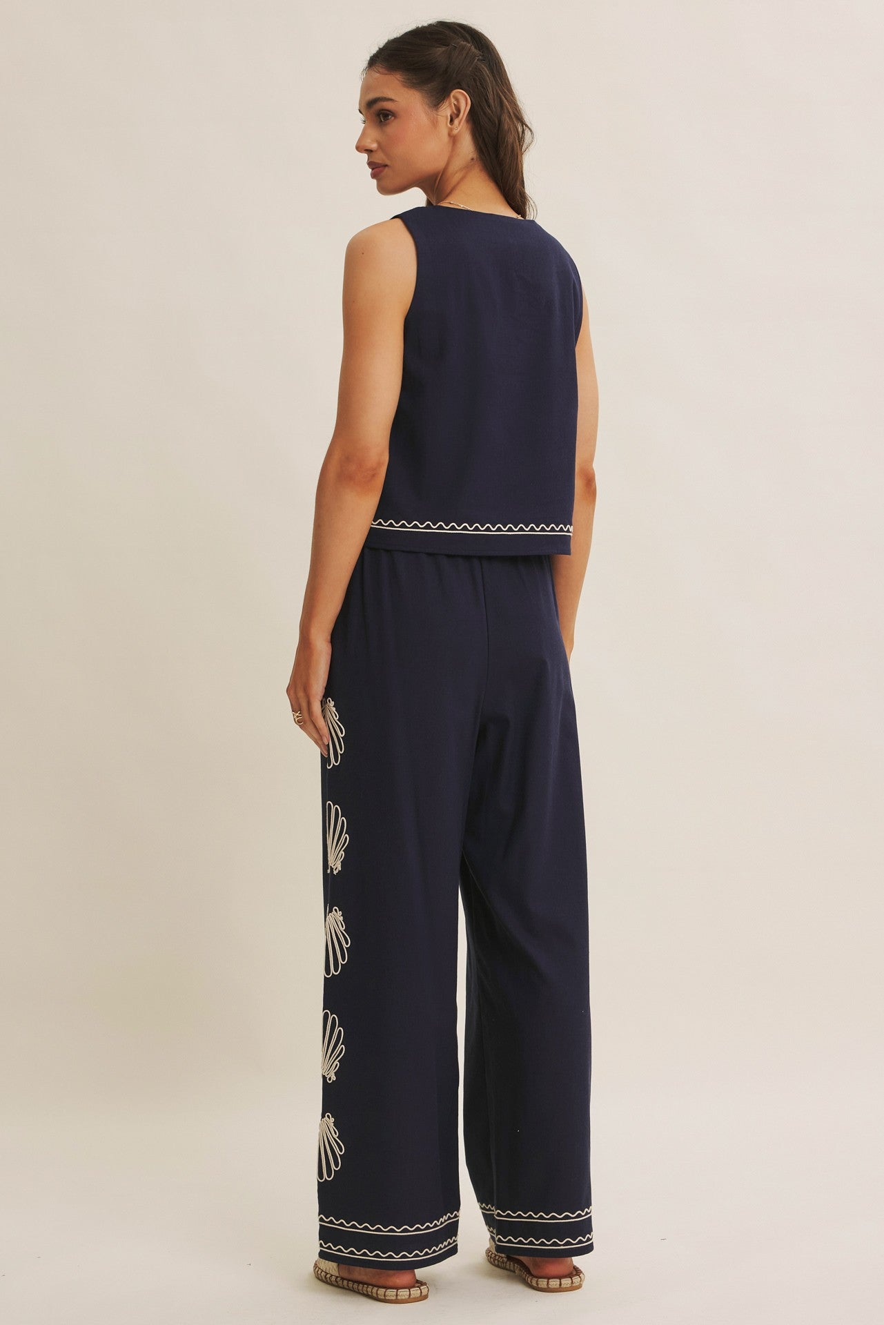 Woman wearing a navy blue sleeveless top and wide-leg pants with white embroidery on a beige background