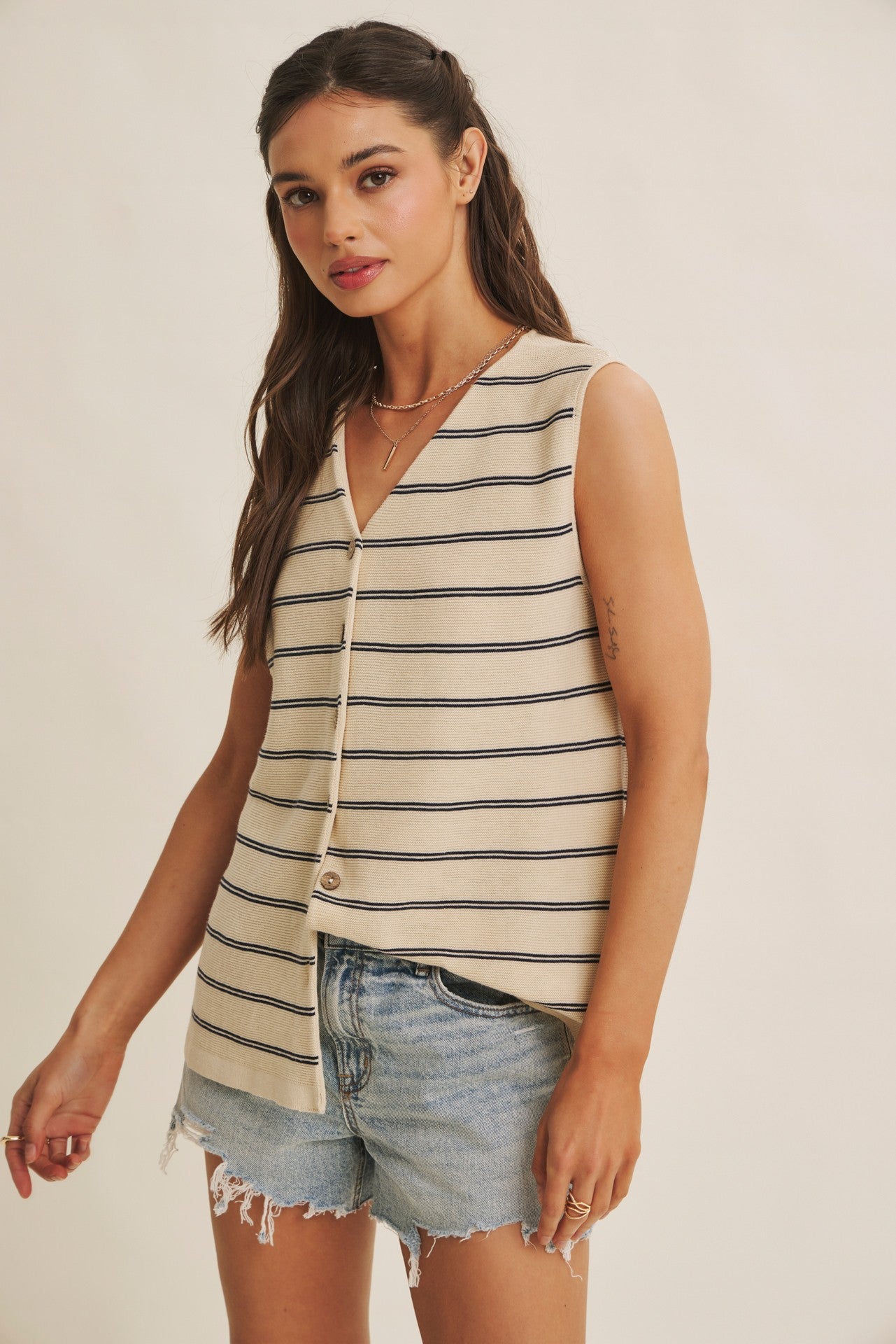 Woman wearing a striped sleeveless top and denim shorts on a plain background