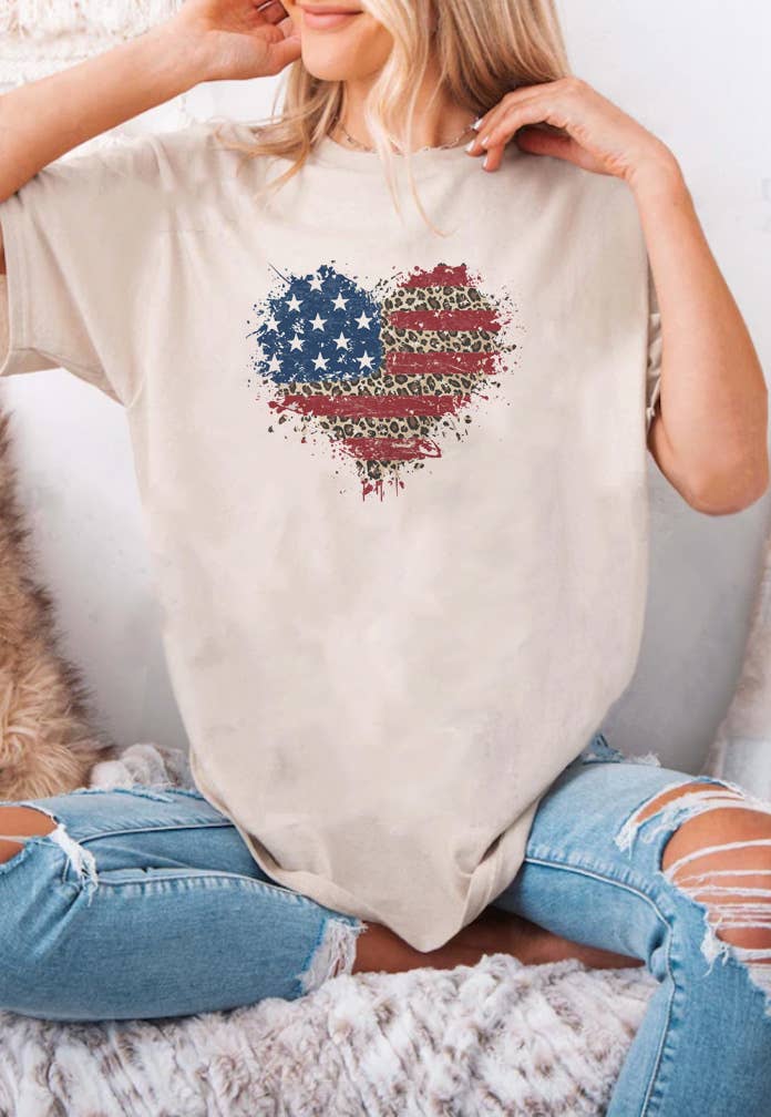 Person wearing a beige t-shirt with an American flag heart design, sitting on a textured surface.