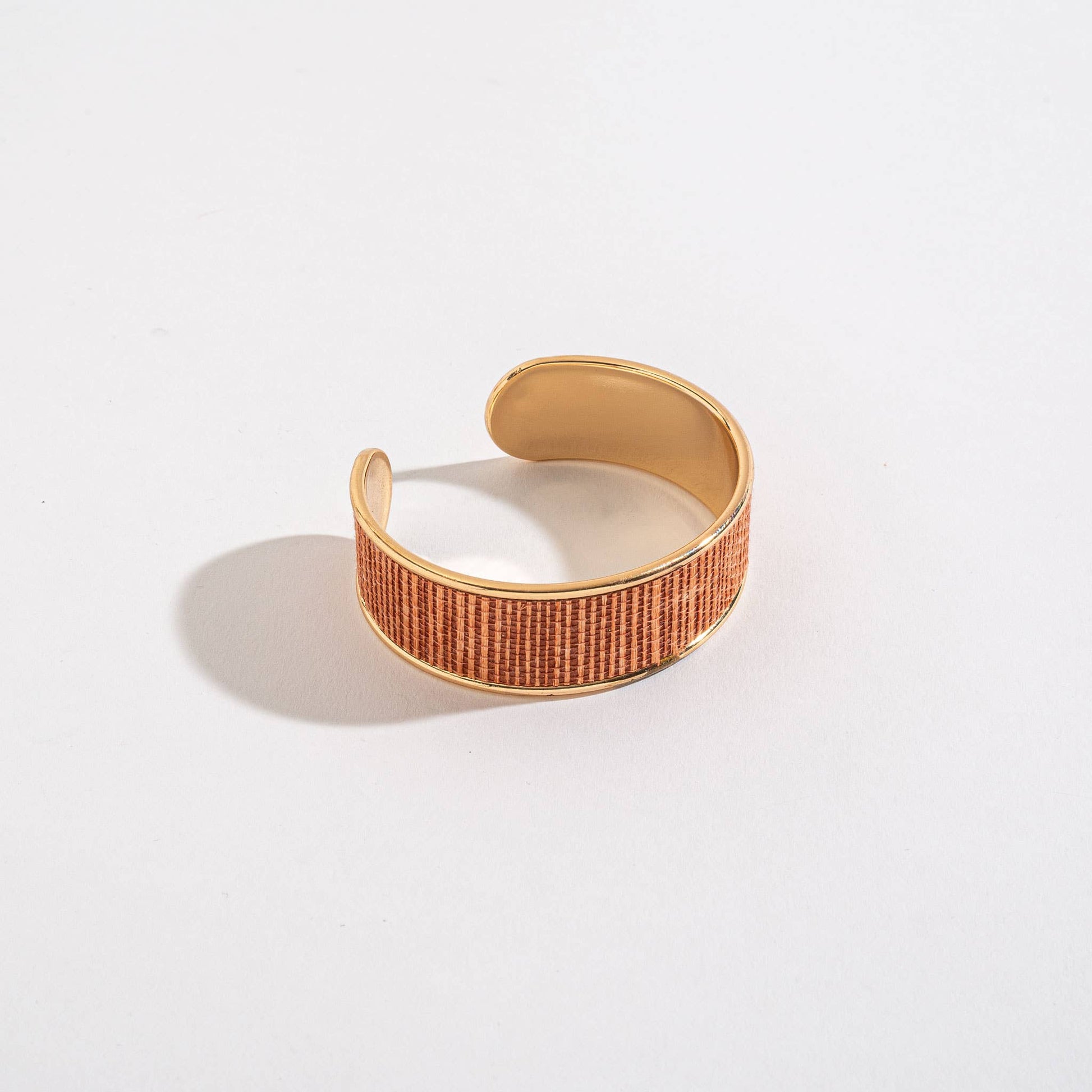 Gold and brown woven cuff bracelet on a light gray background