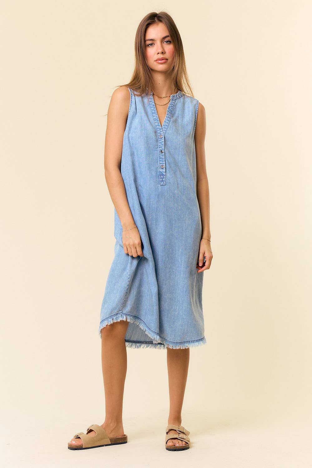 Woman wearing a light blue denim dress against a beige background