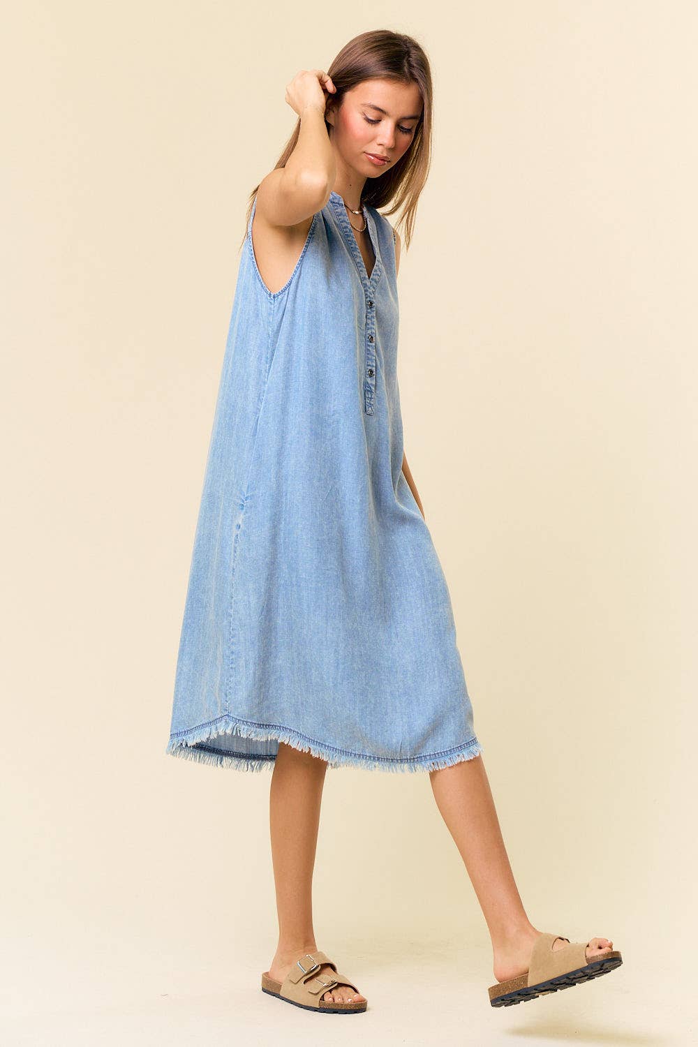Woman wearing a light blue denim dress against a beige background