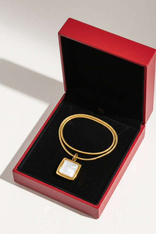 Gold necklace with a rectangular pendant on a white background