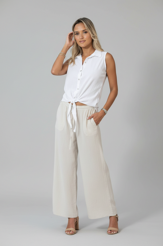 Woman wearing a white sleeveless shirt and beige pants on a gray background