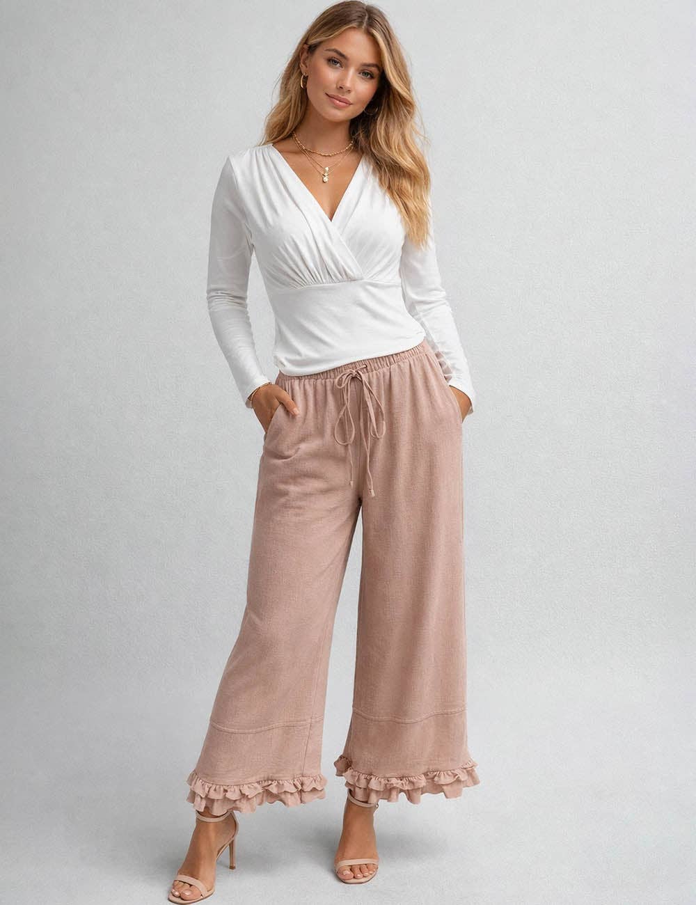 Woman wearing a white long-sleeve top and pink pants on a gray background