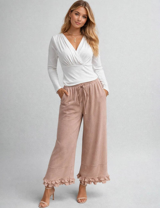 Woman wearing a white long-sleeve top and pink pants on a gray background