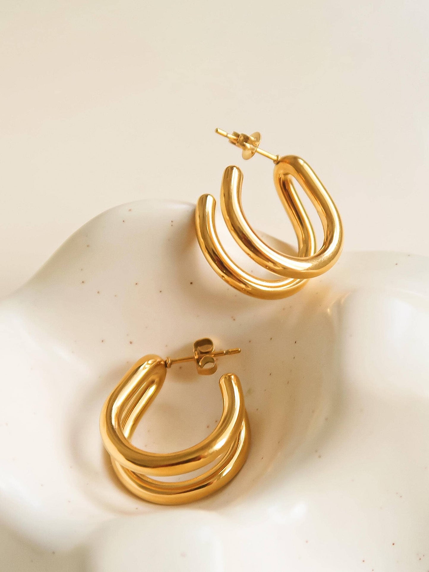 Gold hoop earrings on a textured beige surface