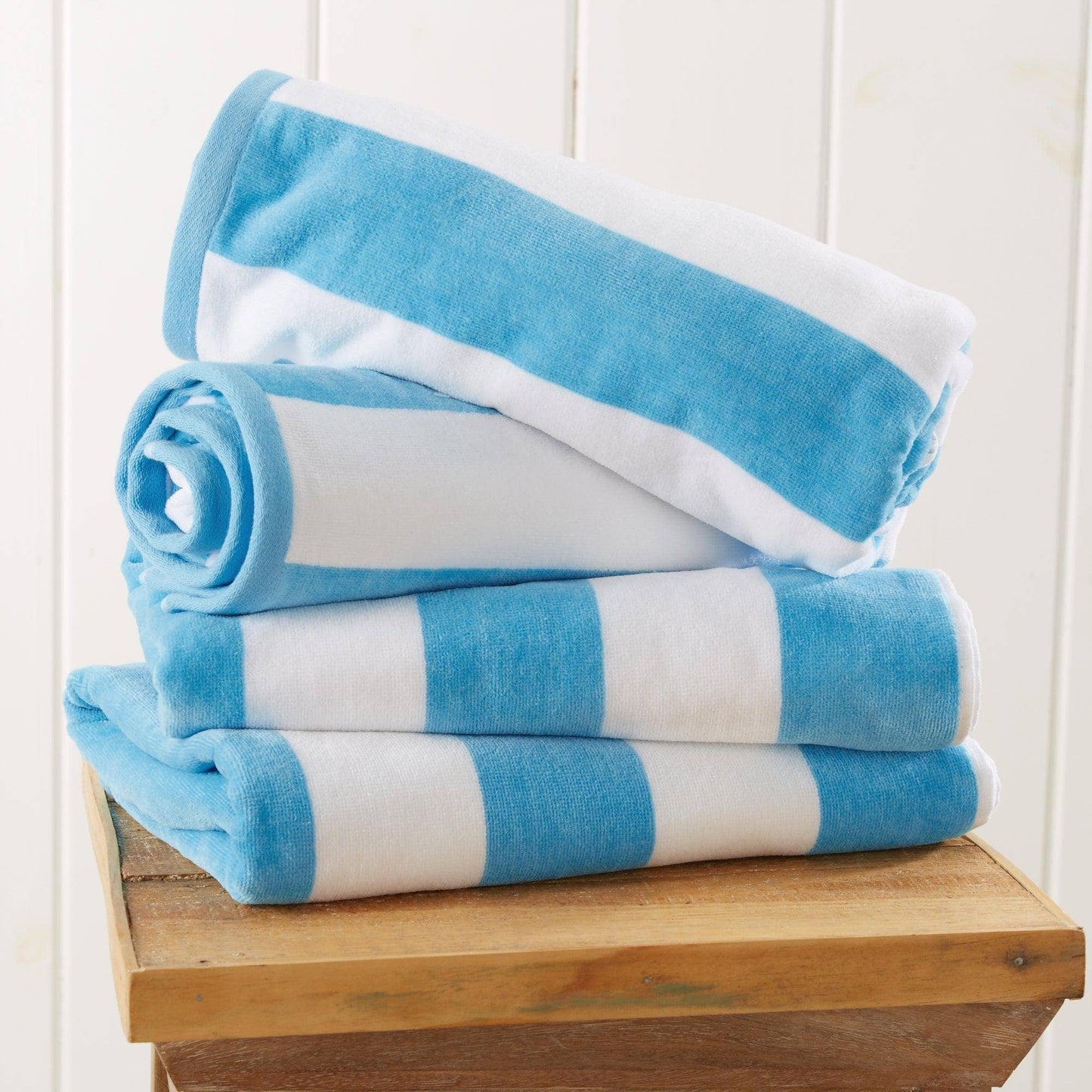 Stack of blue and white striped towels on a wooden surface with a white background