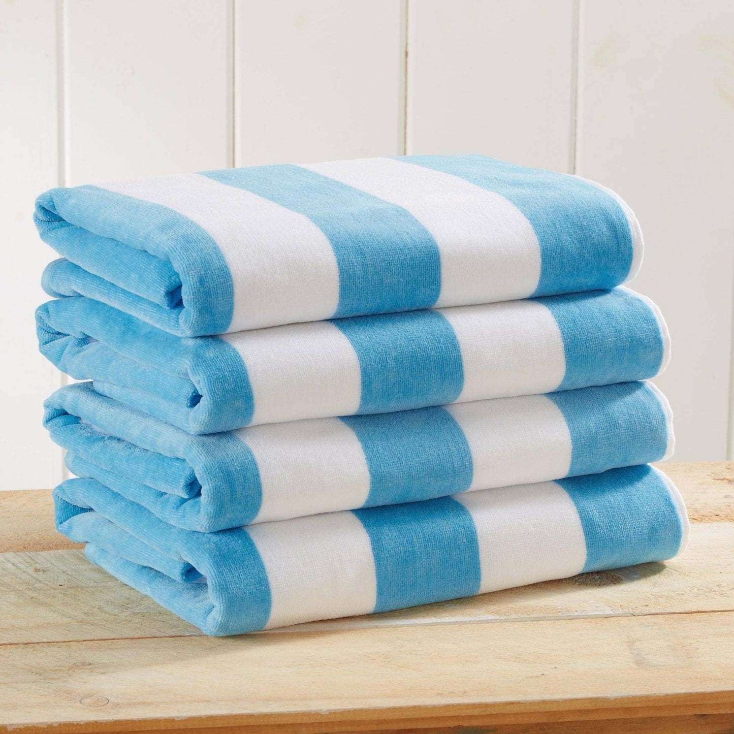 Stack of blue and white striped towels on a wooden surface with a white paneled wall background.