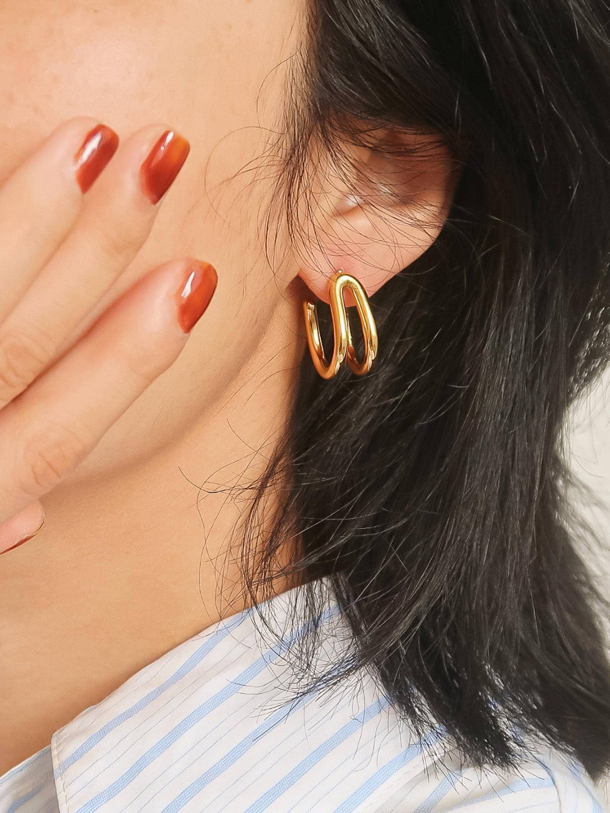 Close-up of a person wearing gold hoop earrings with a neutral background