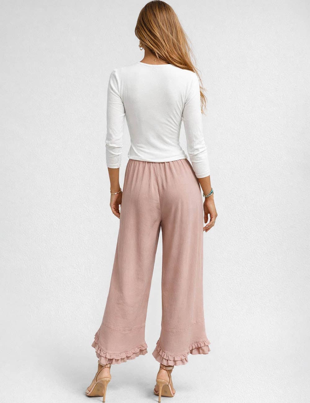 Woman wearing a white long-sleeve top and pink wide-leg pants on a light gray background