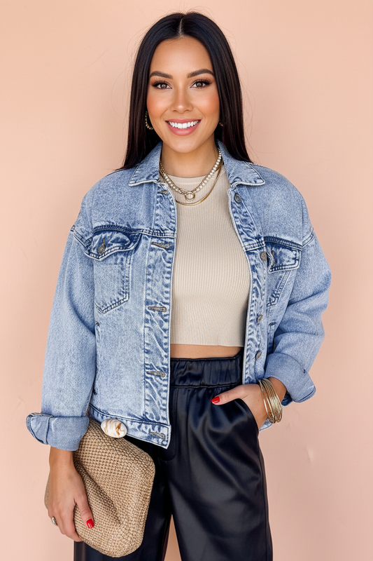 Woman wearing a denim jacket, beige top, and black pants against a beige background