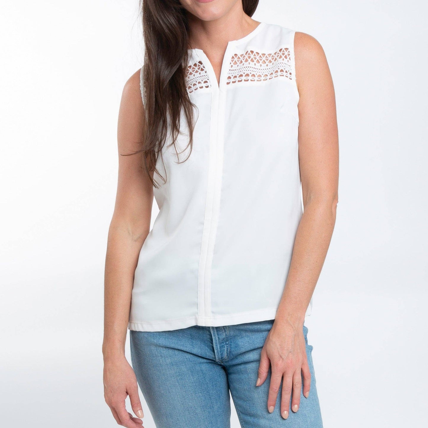 Woman wearing a white sleeveless top with lace details and blue jeans on a white background