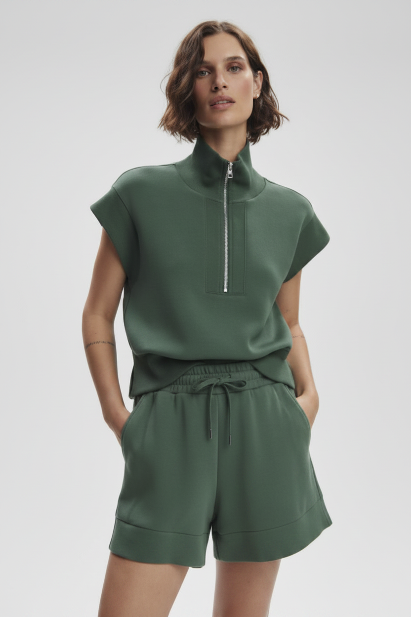 Woman wearing a green outfit with a high collar and shorts on a light gray background
