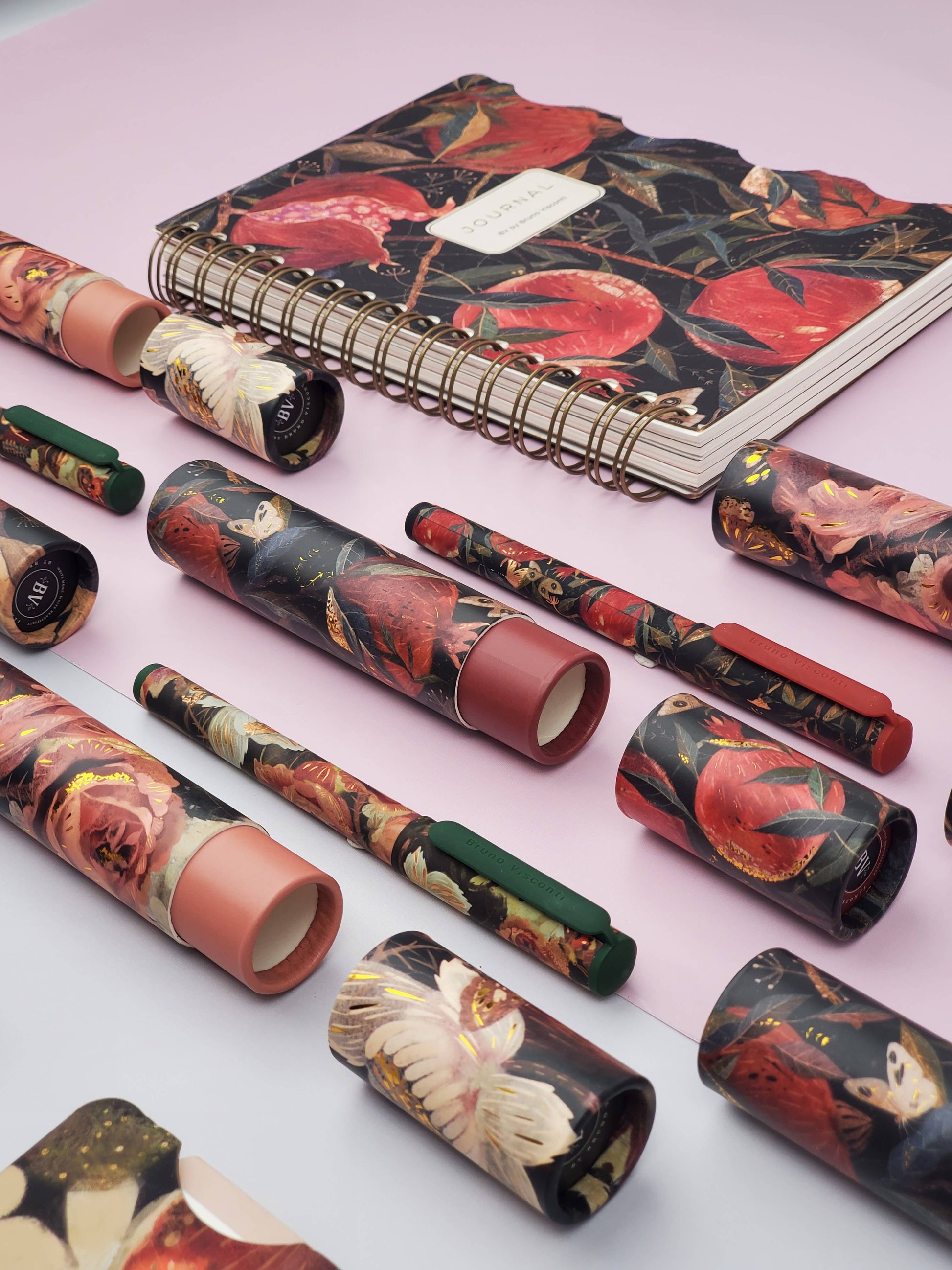 Set of pens and notebooks with floral designs on a light pink background