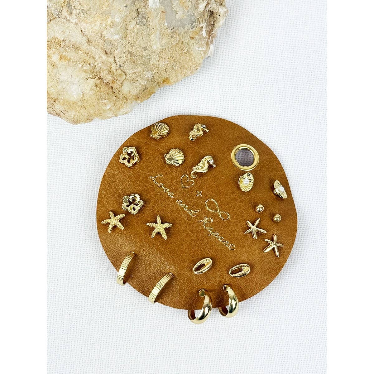Round brown leather earring holder with gold earrings on a white background