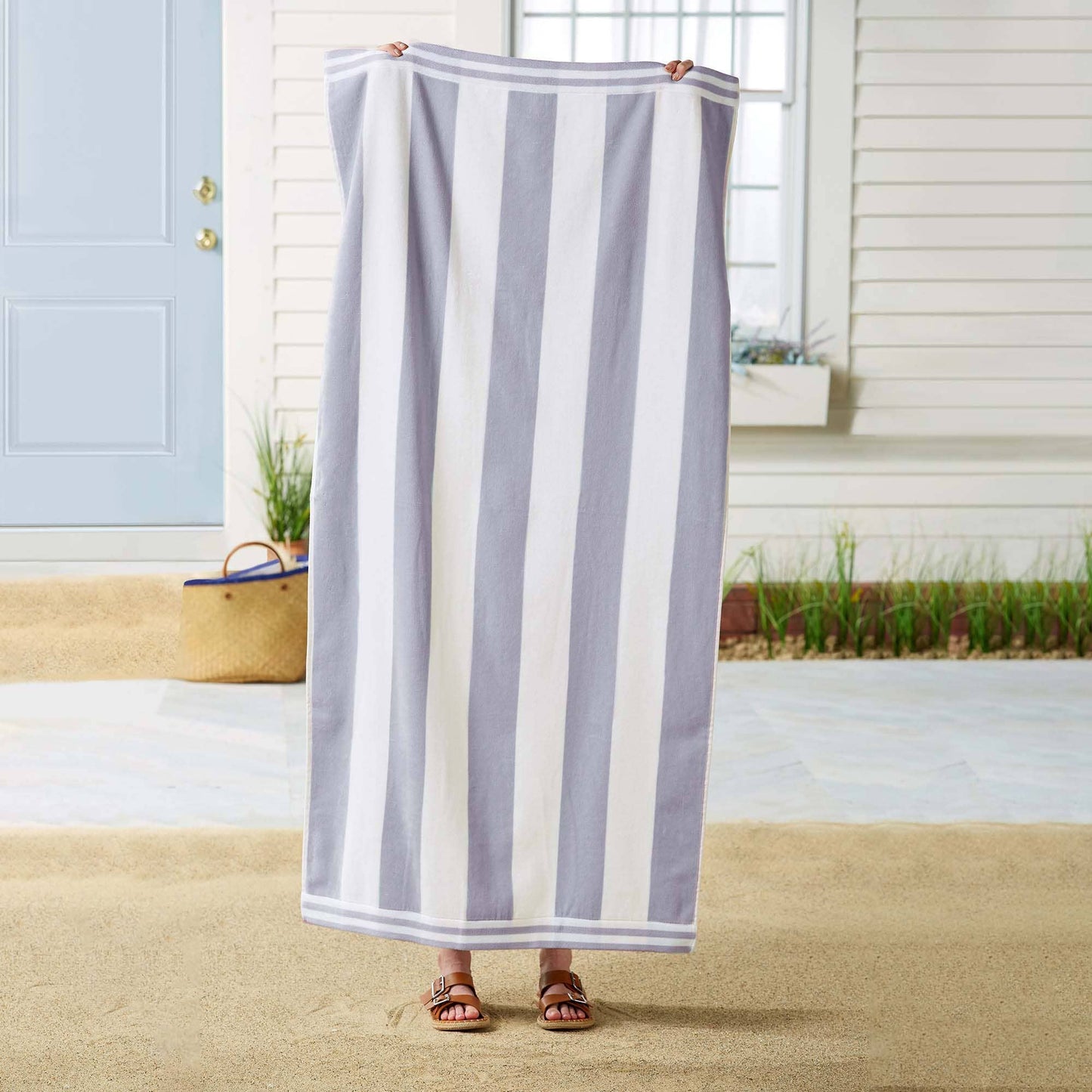 Person holding a striped towel in front of a house with a blue door.