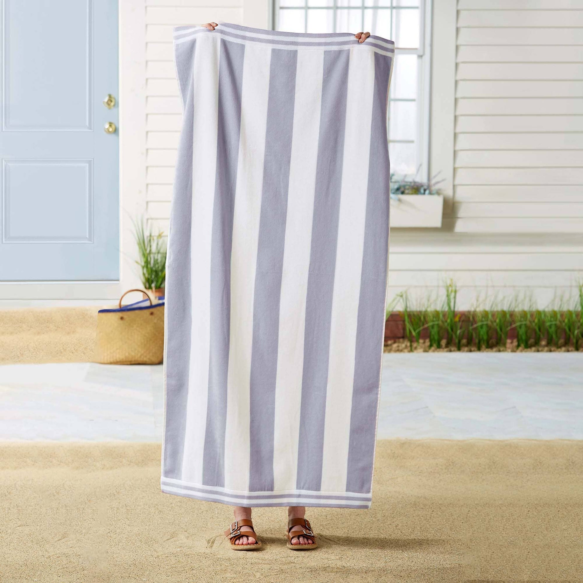 Person holding a striped towel in front of a house with a blue door.