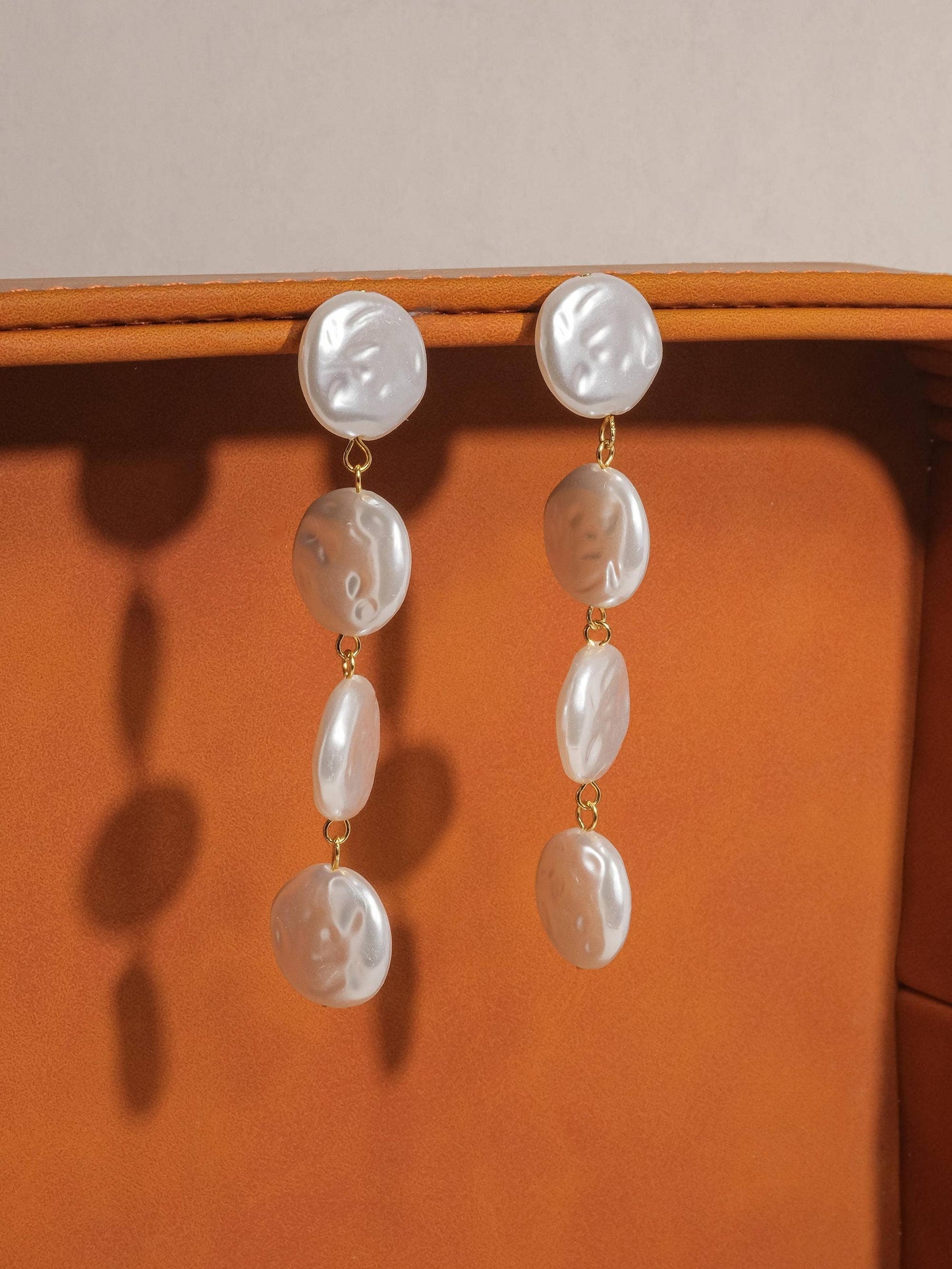Pearl earrings hanging on a wooden surface with a neutral background