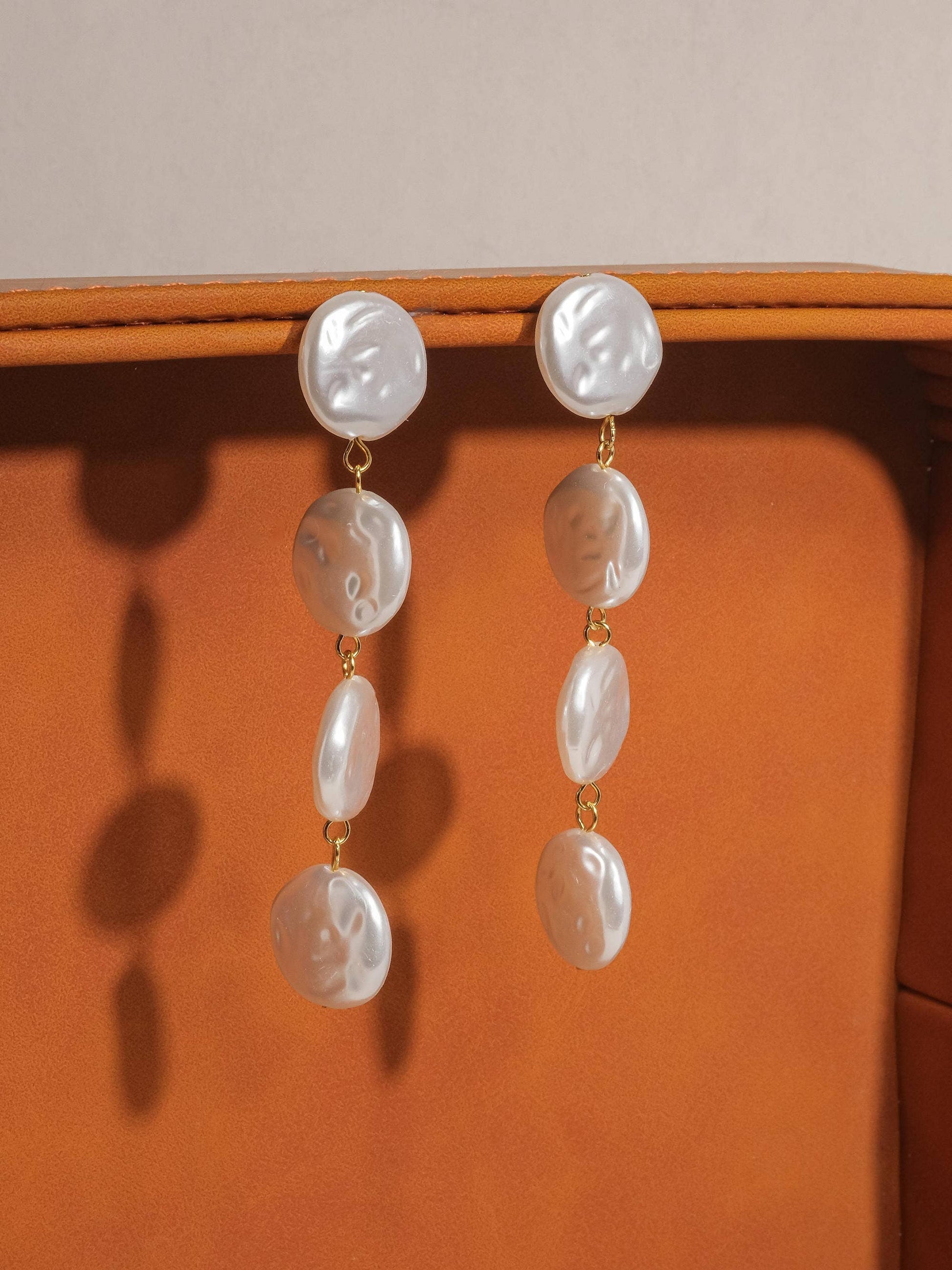 Pearl earrings hanging on a wooden surface with a neutral background