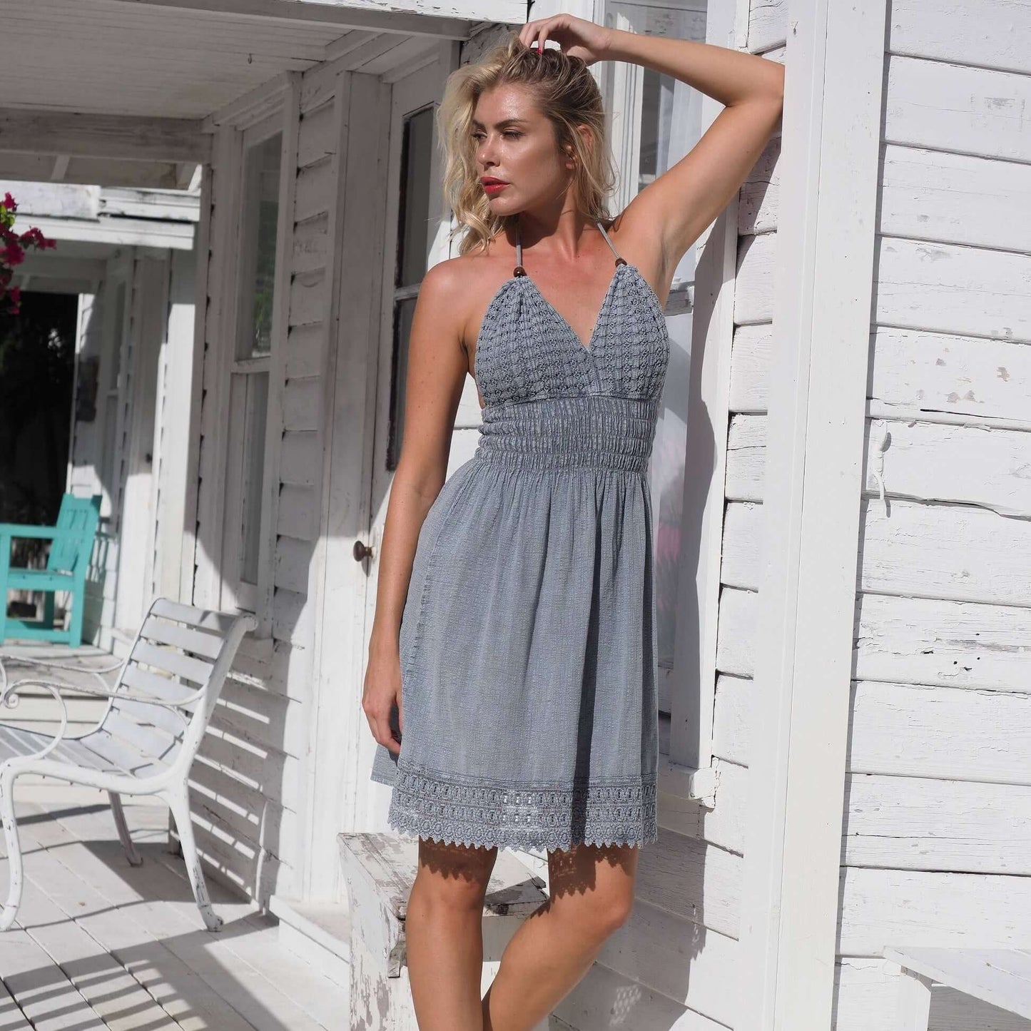Woman in a light blue dress standing on a white porch.