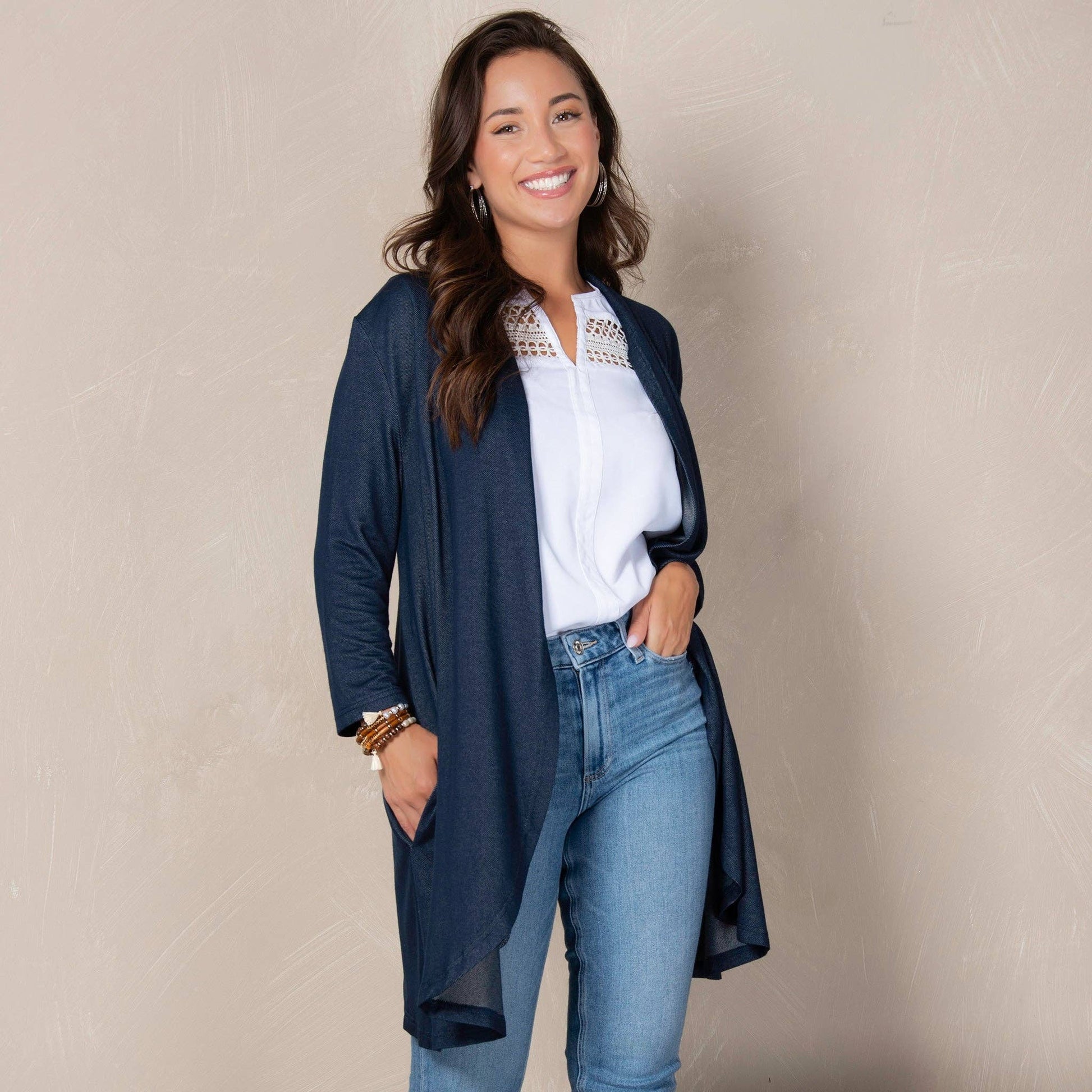 Woman wearing a navy cardigan, white blouse, and blue jeans against a beige background
