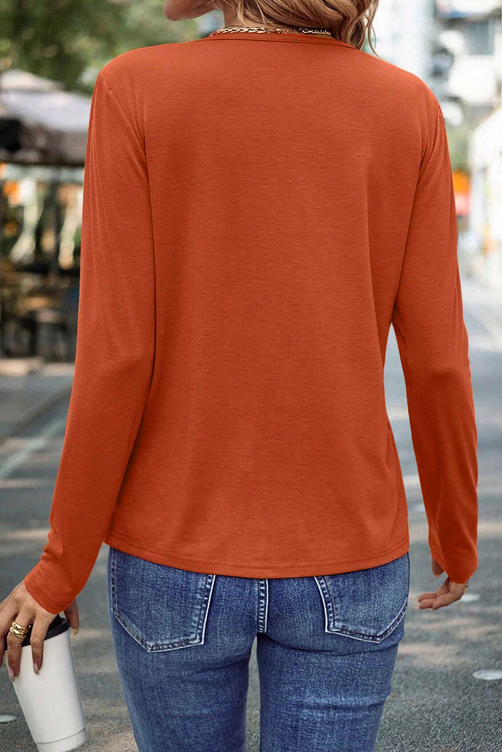 Person wearing an orange long-sleeve top and blue jeans, standing on a street.