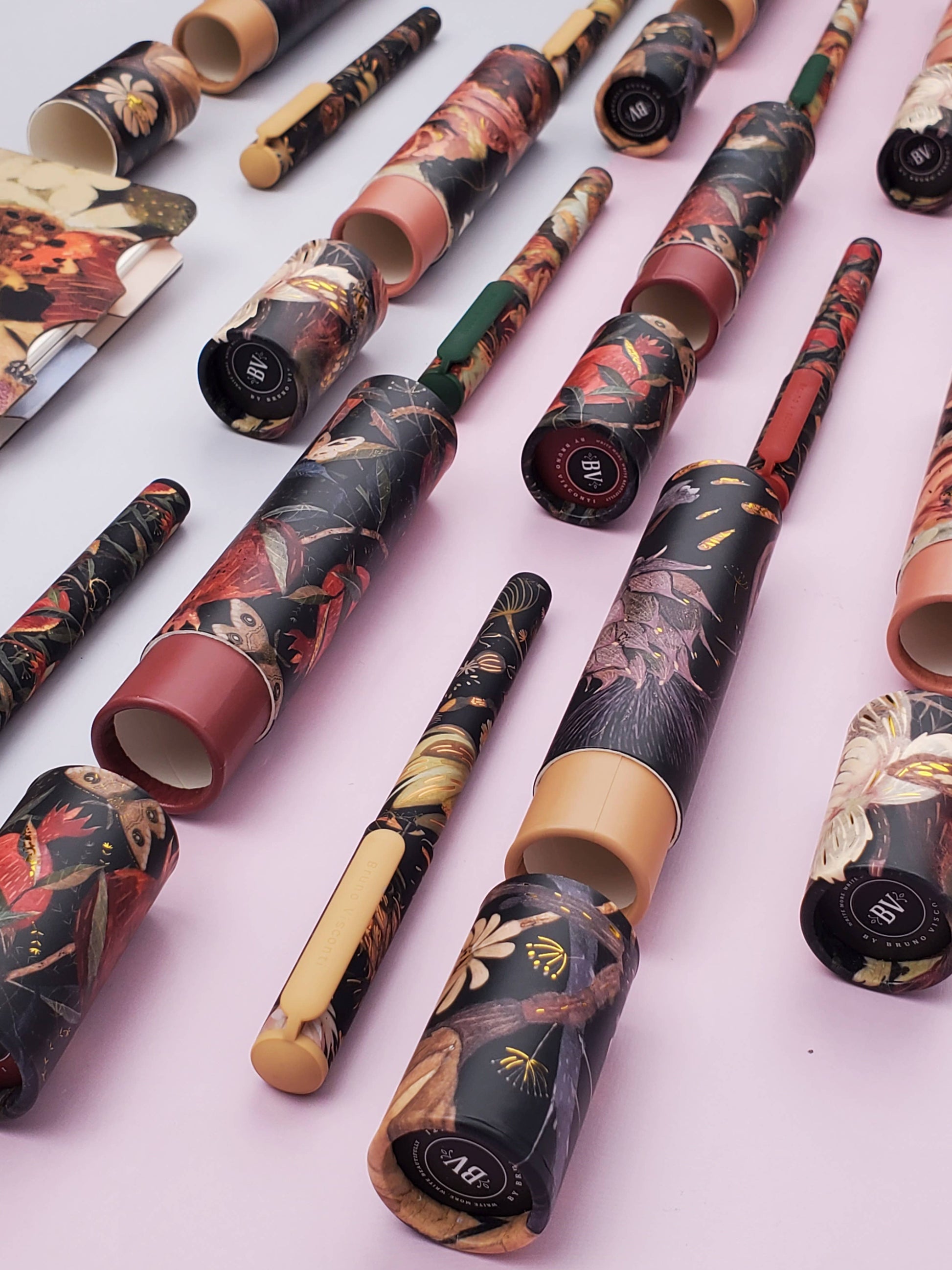 Collection of intricately designed pens and writing instruments on a light pink background