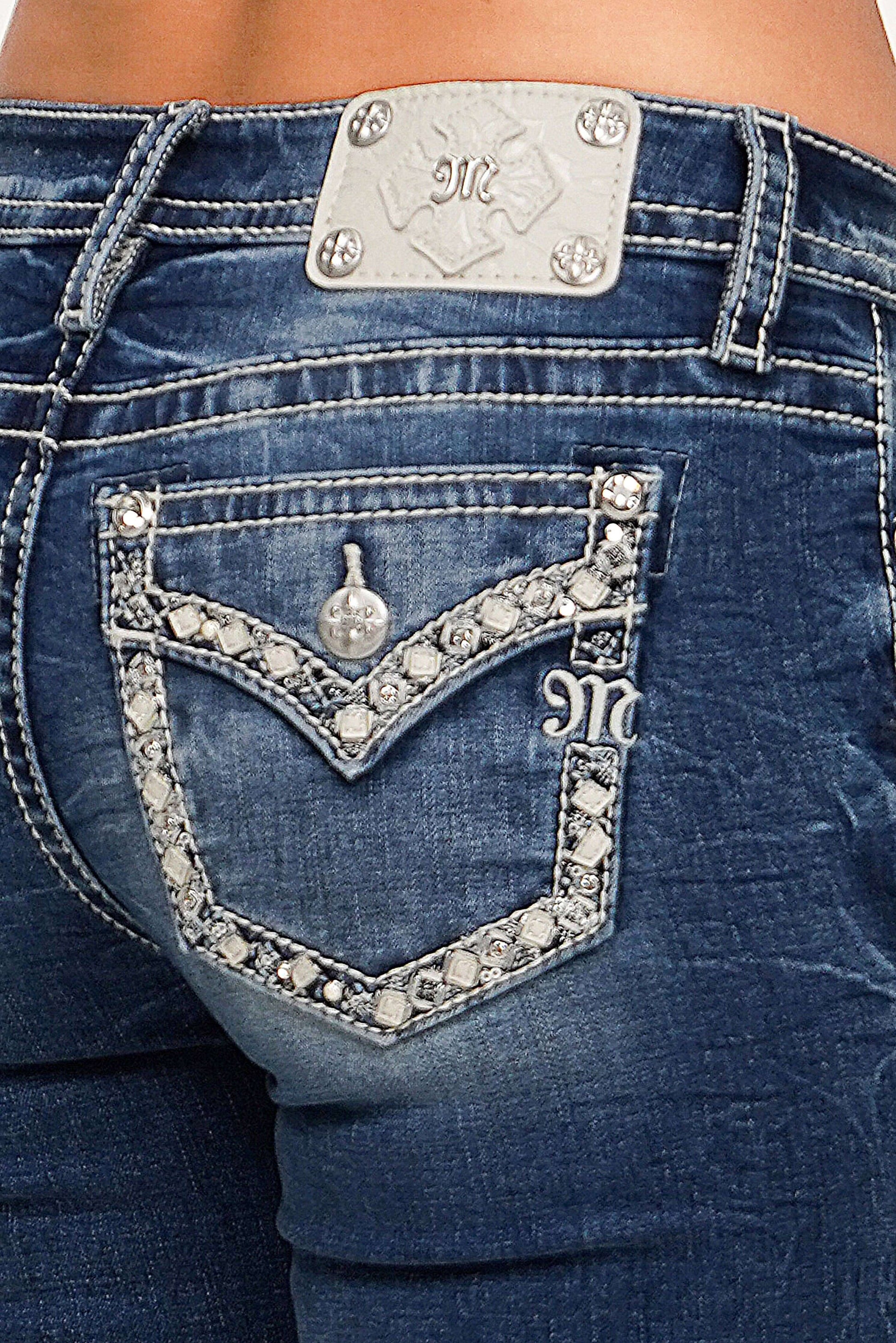 Close-up of blue jeans with decorative embellishments and a brand logo.