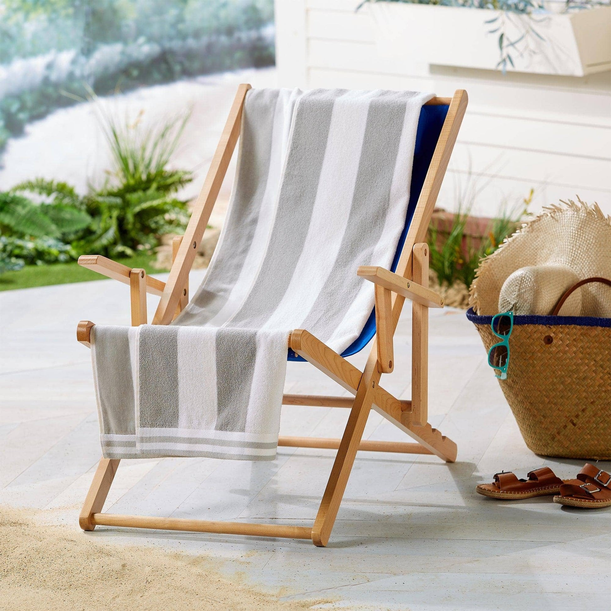 Wooden beach chair with striped towel and straw bag on a sandy surface