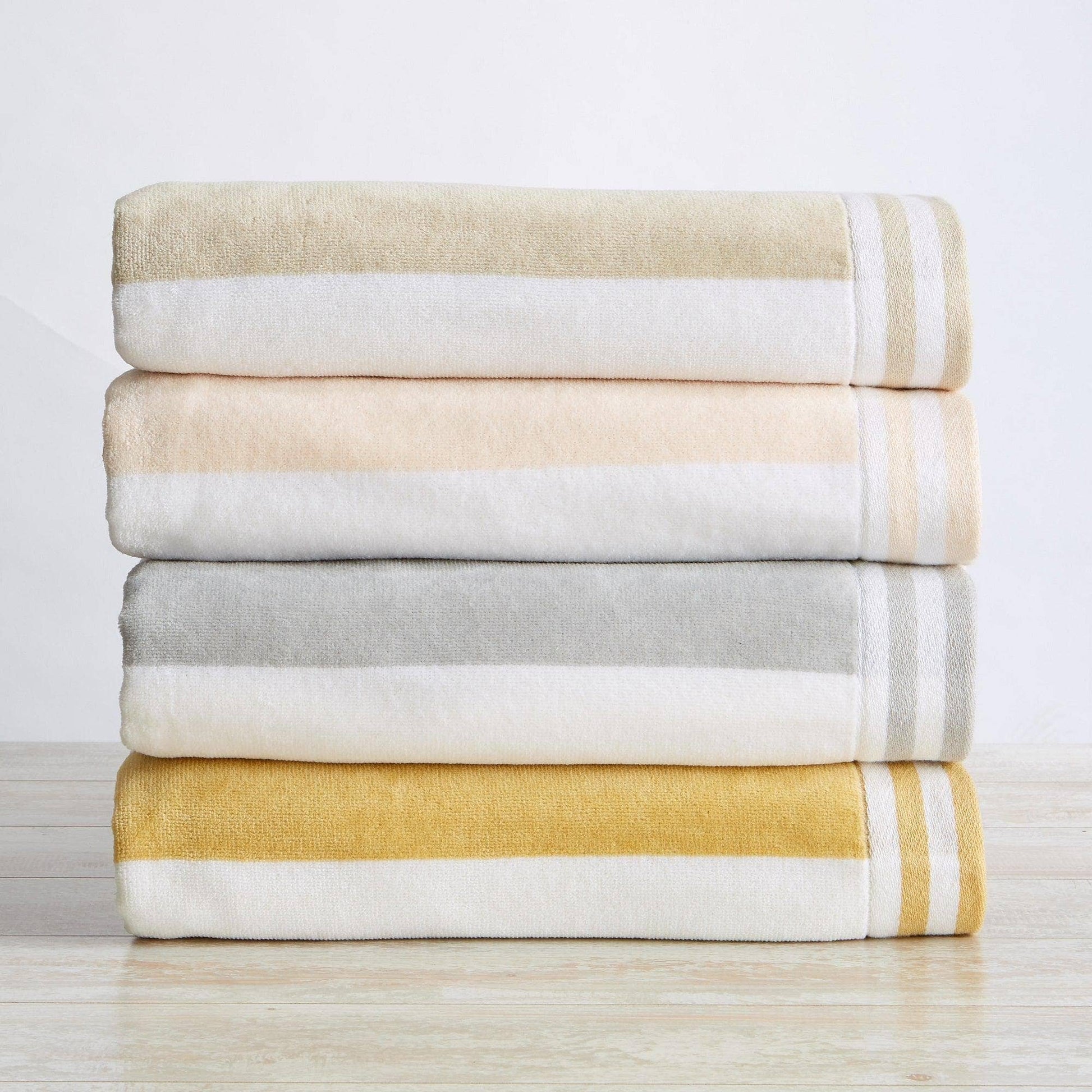 Stack of folded towels in beige, white, gray, and yellow on a light wooden surface.