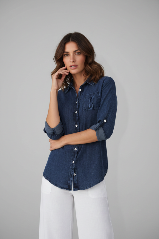 Woman wearing a blue denim shirt and white pants against a gray background
