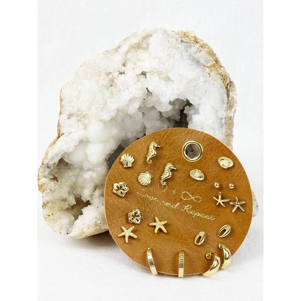 Set of gold earrings on a wooden display card with a white geode background