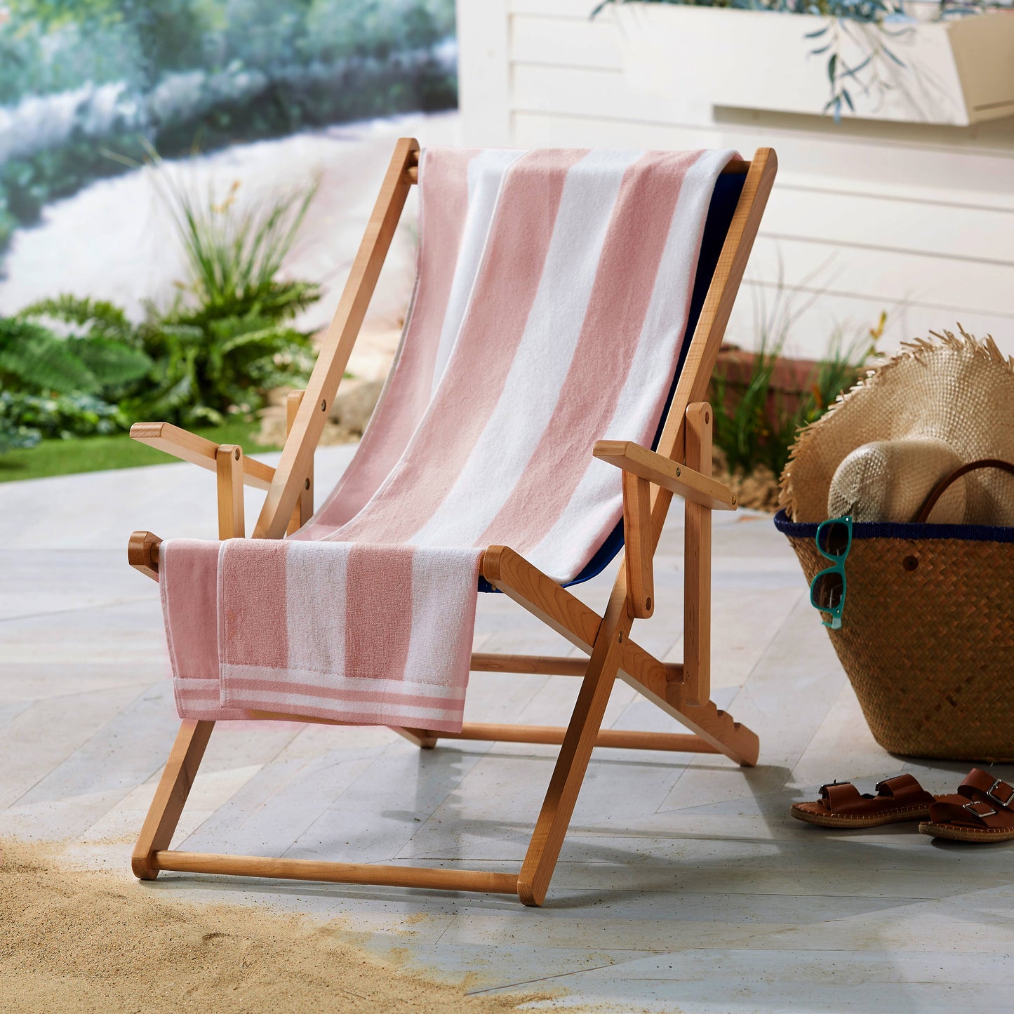 Wooden deck chair with a pink and white striped towel on a patio.