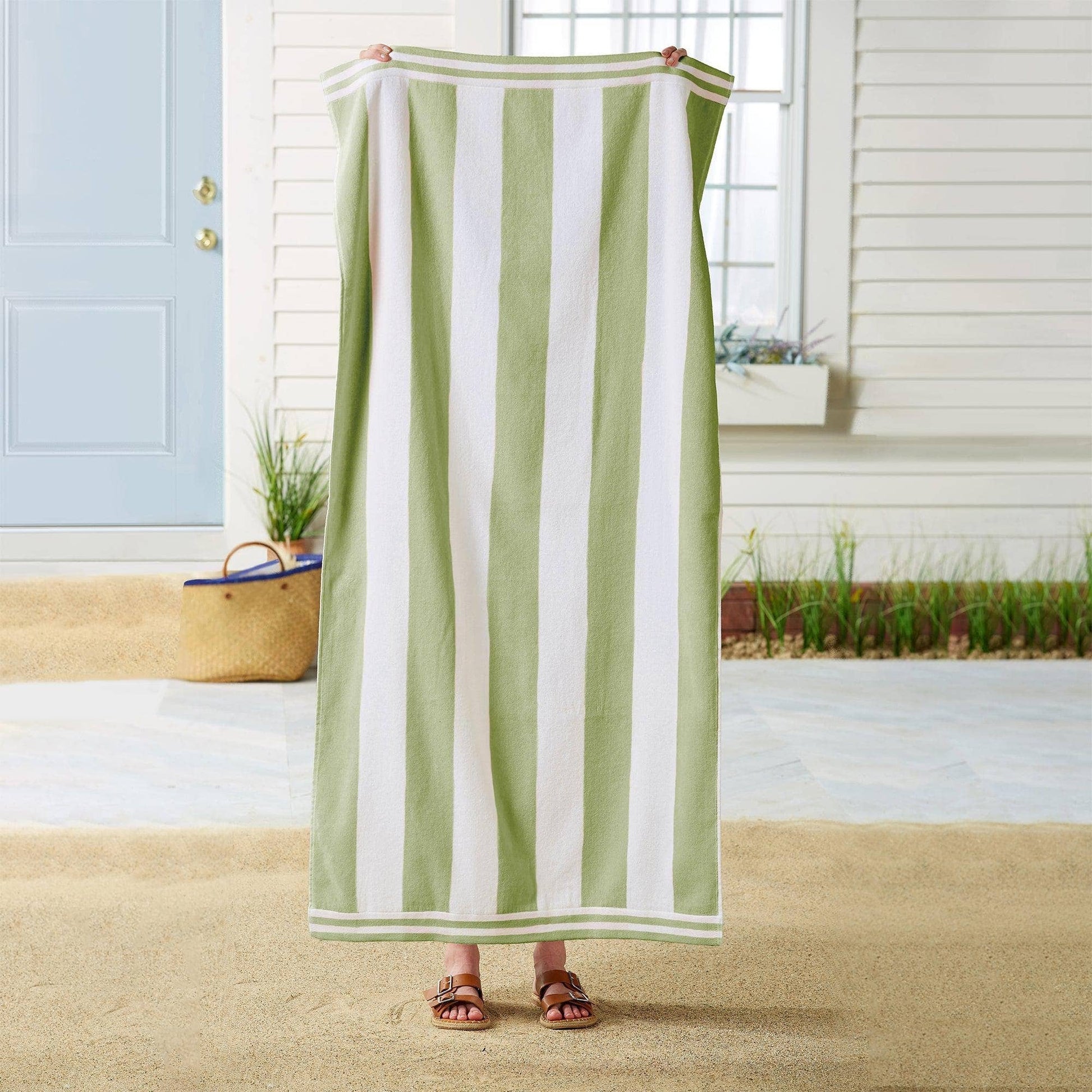 Person holding a green and white striped towel on a sandy beach.