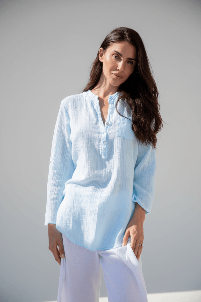 Woman wearing a light blue shirt and white pants against a gray background