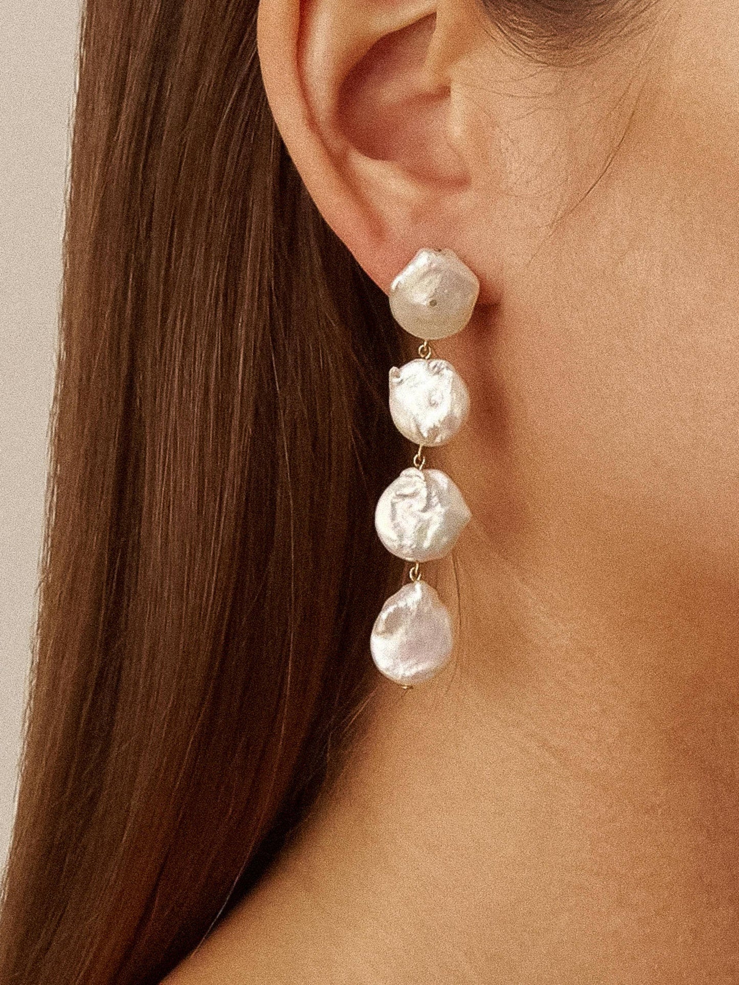 Pearl earring worn by a person with long hair, close-up shot.