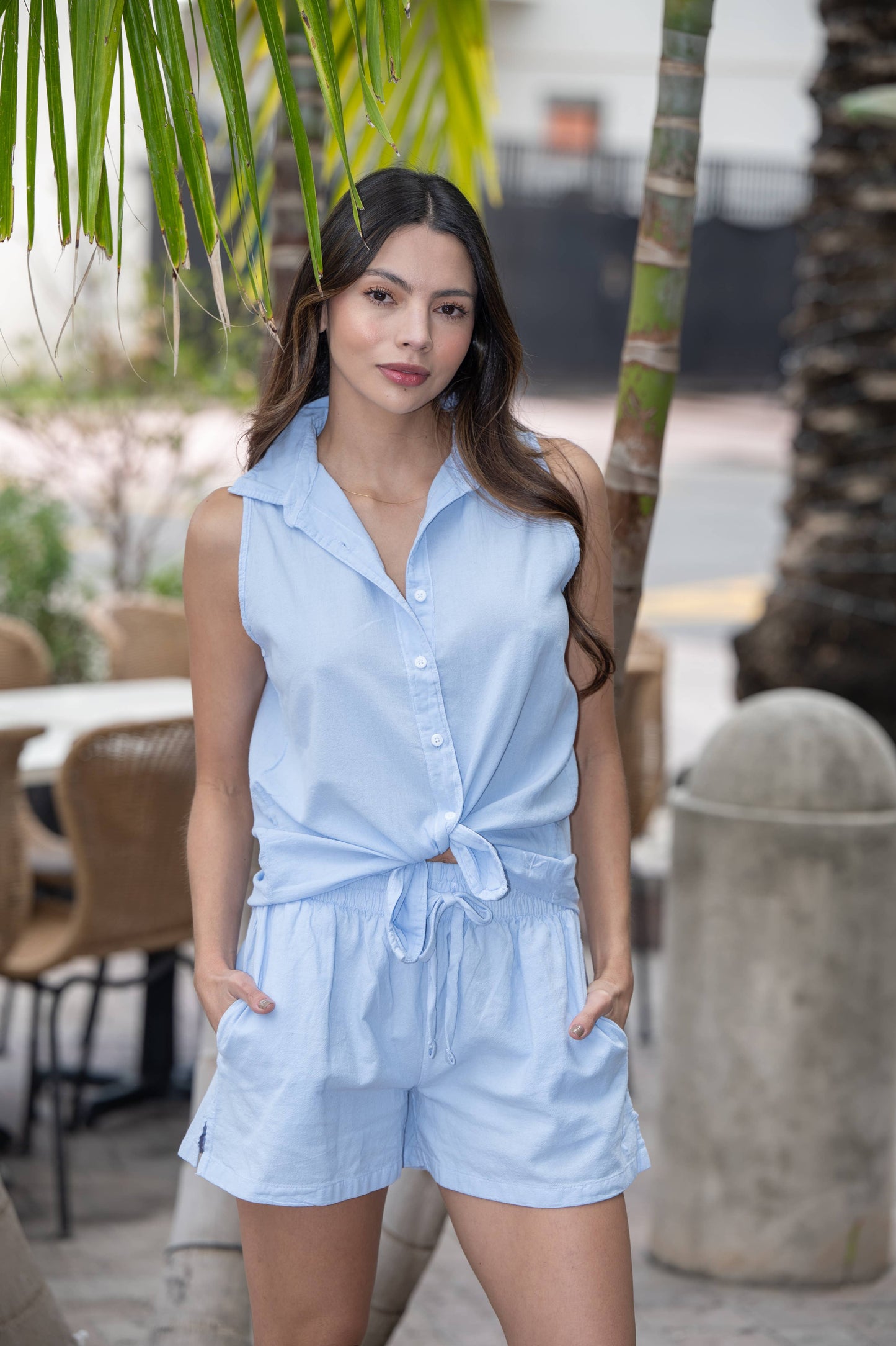 Woman wearing a light blue romper standing outdoors with palm trees in the background