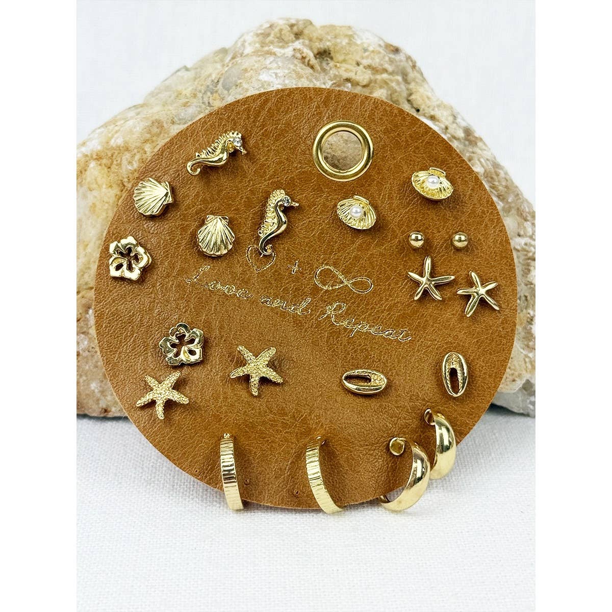 Collection of gold sea-themed earrings on a brown leather display pad.