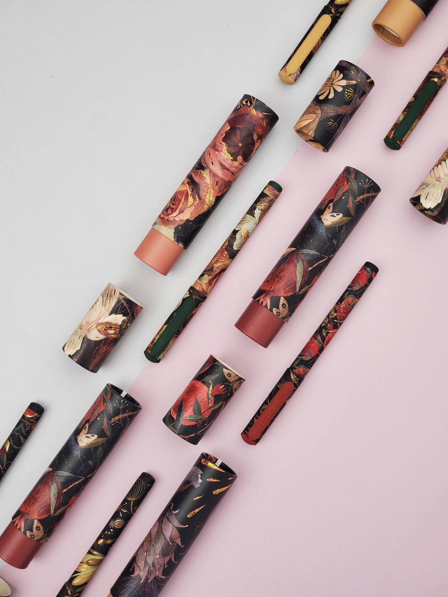 Decorative lip gloss tubes with floral designs on a pink and gray background