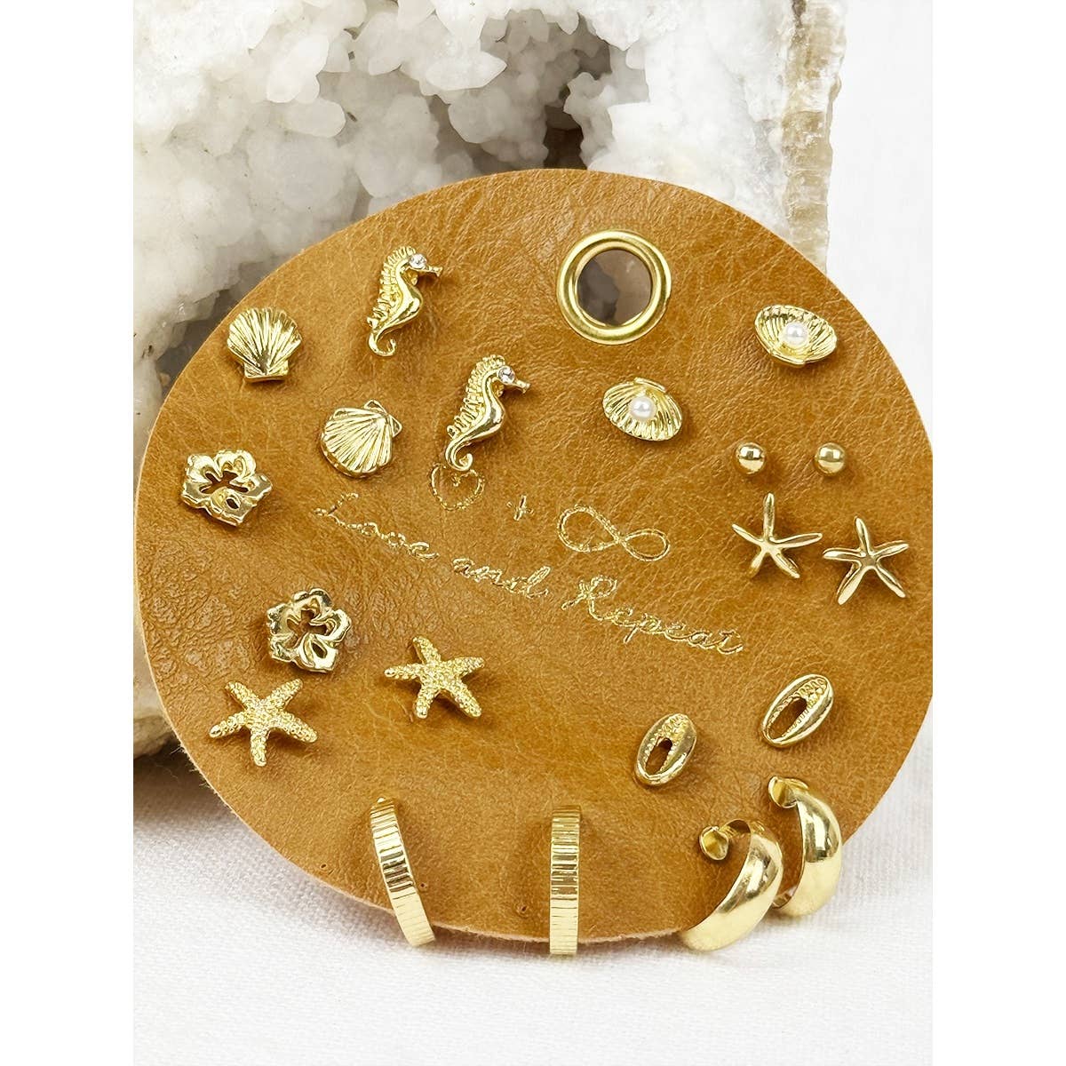 Collection of gold sea-themed earrings on a wooden display with 'Lover and Keeper' engraving.